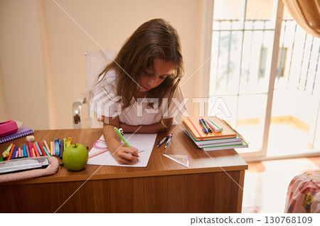 Young Girl Studying at Desk with Stationery in a Bright Room 130768109