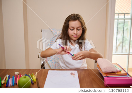 Young Girl Sharpening Colored Pencil at Desk with School Supplies 130768113