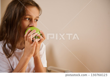 Young Girl Eating a Green Apple While Sitting Indoors Young Girl Eating a Green Apple While Sitting Indoors 130768123