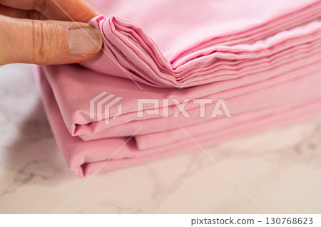 A close-up shot of pink bedsheets folded neatly into layers. The soft pastel color and fabric texture are emphasized. A close-up shot of pink bedsheets folded neatly into layers. The soft pastel color and fabric texture are emphasized. 130768623