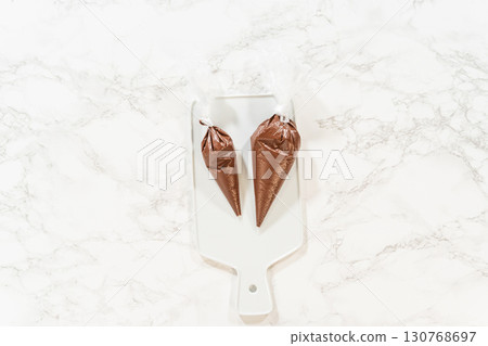 Piping Bags on Cooling Rack Description: Overhead view of piping bags filled with melted chocolate resting on a cooling rack, prepared for the Chocolate Royal Icing recipe. Piping Bags on Cooling Rack Description: Overhead view of piping bags filled with melted chocolate resting on a cooling rack, prepared for the Chocolate Royal Icing recipe. 130768697