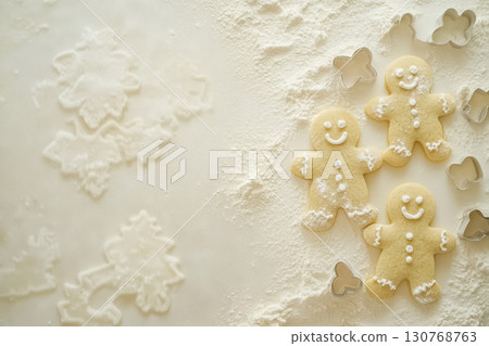 Three smiling gingerbread cookies on a surface dusted with flour, surrounded by cookie cutters and embossed dough patterns. A charming holiday baking scene suitable for Christmas recipe or DIY cookie 130768763
