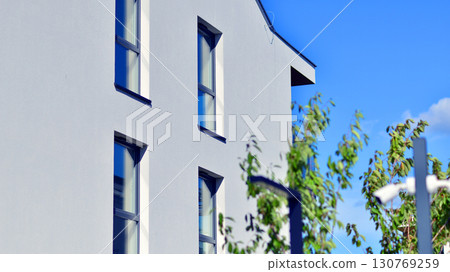 Modern apartment building with balconies and greenery. Beautiful view of real estate buildings in summer. Walking area with trees and grass. Modern residential buildings in the public green area.  130769259