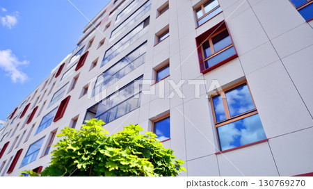 Modern apartment building with balconies and greenery. Beautiful view of real estate buildings in summer. Walking area with trees and grass. Modern residential buildings in the public green area.  130769270
