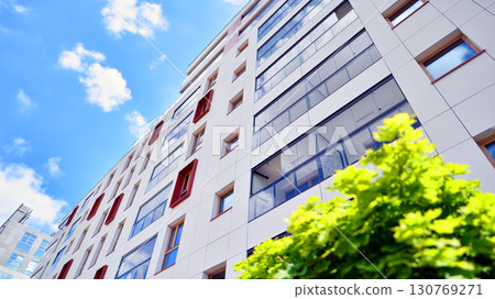 Modern apartment building with balconies and greenery. Beautiful view of real estate buildings in summer. Walking area with trees and grass. Modern residential buildings in the public green area.  130769271