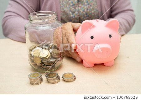 Retired elderly woman counting coins money with piggy bank and worry about monthly expenses and treatment fee payment. 130769529