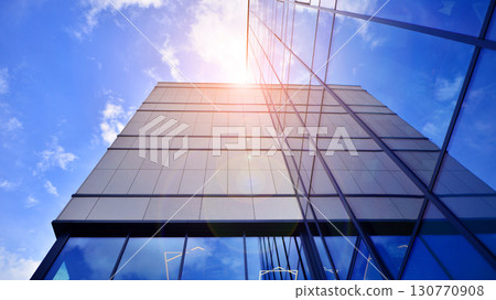 Modern office building with glass facade. Transparent glass wall of office building. Reflection of the blue sky on the facade of the building. 130770908