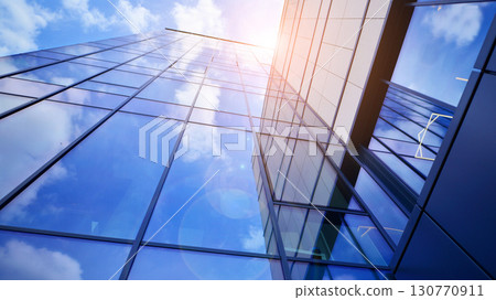 Modern office building with glass facade. Transparent glass wall of office building. Reflection of the blue sky on the facade of the building. Modern office building with glass facade. Transparent glass wall of office building. Reflection of the blue sky on the facade of the building. 130770911