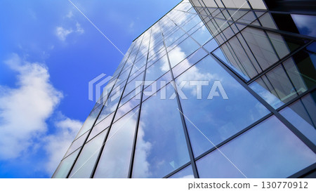 Modern office building with glass facade. Transparent glass wall of office building. Reflection of the blue sky on the facade of the building. 130770912
