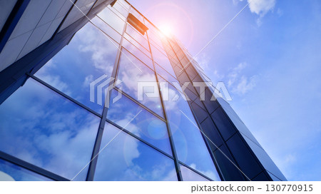 Modern office building with glass facade. Transparent glass wall of office building. Reflection of the blue sky on the facade of the building. Modern office building with glass facade. Transparent glass wall of office building. Reflection of the blue sky on the facade of the building. 130770915