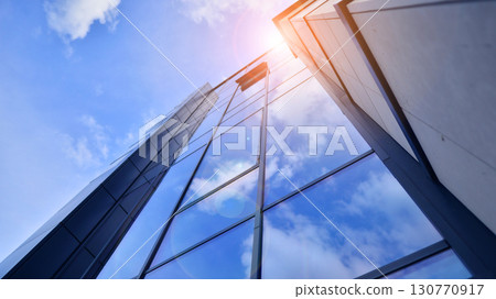 Modern office building with glass facade. Transparent glass wall of office building. Reflection of the blue sky on the facade of the building. 130770917