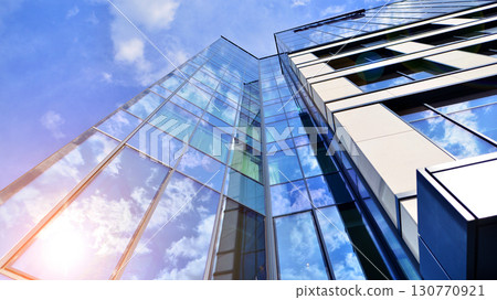 Modern office building with glass facade. Transparent glass wall of office building. Reflection of the blue sky on the facade of the building. 130770921
