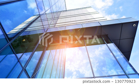 Modern office building with glass facade. Transparent glass wall of office building. Reflection of the blue sky on the facade of the building. Modern office building with glass facade. Transparent glass wall of office building. Reflection of the blue sky on the facade of the building. 130770923