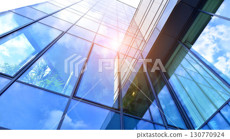 Modern office building with glass facade. Transparent glass wall of office building. Reflection of the blue sky on the facade of the building. 130770924