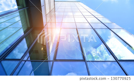 Modern office building with glass facade. Transparent glass wall of office building. Reflection of the blue sky on the facade of the building. 130770925