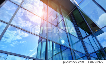 Modern office building with glass facade. Transparent glass wall of office building. Reflection of the blue sky on the facade of the building. Modern office building with glass facade. Transparent glass wall of office building. Reflection of the blue sky on the facade of the building. 130770927