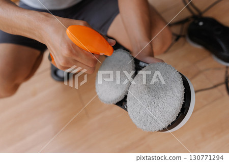 Close-up cropped shot of unrecognizable cleaning company worker preparing automatic cleaning robot by spraying detergent on cleaning pads, ensuring streak-free and efficient window cleaning. 130771294
