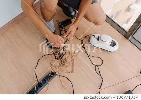 Window cleaner male preparing automatic window cleaning robot while tying cables with rope on floor, organizing equipment and getting ready for day tasks. Concept of cleaning house with smart devices. Window cleaner male preparing automatic window cleaning robot while tying cables with rope on floor, organizing equipment and getting ready for day tasks. Concept of cleaning house with smart devices. 130771317