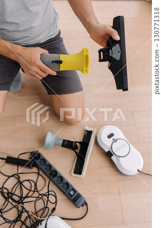 Janitor male preparing cordless window cleaning appliances and robot vacuum cleaner for cleaning large window in office building, focus on window cleaning tools. Concept of household cleanliness. Janitor male preparing cordless window cleaning appliances and robot vacuum cleaner for cleaning large window in office building, focus on window cleaning tools. Concept of household cleanliness. 130771318