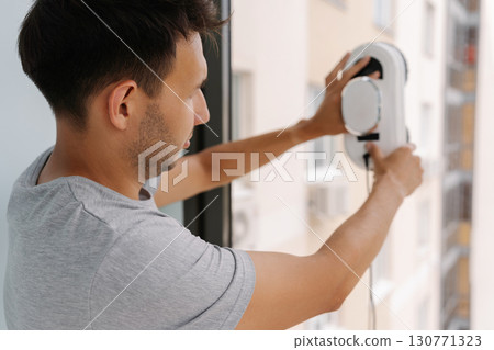 Close-up back view of cleaning service employee mounting advanced window washing robot on skyscraper exterior, performing high-altitude maintenance with precision and safety technology. Close-up back view of cleaning service employee mounting advanced window washing robot on skyscraper exterior, performing high-altitude maintenance with precision and safety technology. 130771323