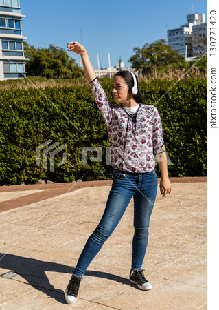 Young latin woman dancing with headphones in urban park Young latin woman dancing with headphones in urban park 130771420