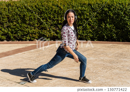 Young woman wearing headphones performing leg stretches in a park 130771422