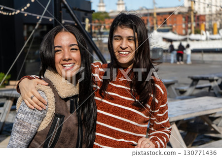Two young women embracing and smiling outdoors 130771436