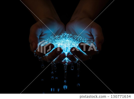 Cupped hands holding magical glowing blue water with dripping light particles on a dark background 130771634