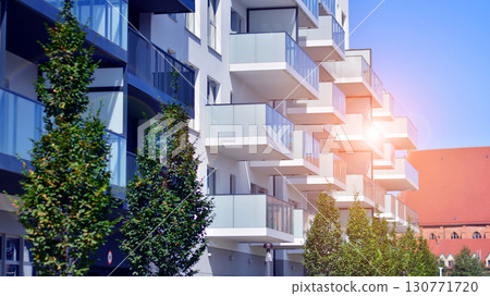 Modern apartment building with balconies and greenery. Beautiful view of real estate buildings in summer. Walking area with trees and grass. Modern residential buildings in the public green area. Modern apartment building with balconies and greenery. Beautiful view of real estate buildings in summer. Walking area with trees and grass. Modern residential buildings in the public green area. 130771720