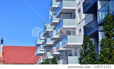 Modern apartment building with balconies and greenery. Beautiful view of real estate buildings in summer. Walking area with trees and grass. Modern residential buildings in the public green area.  130771721
