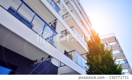 Modern apartment building with balconies and greenery. Beautiful view of real estate buildings in summer. Walking area with trees and grass. Modern residential buildings in the public green area. Modern apartment building with balconies and greenery. Beautiful view of real estate buildings in summer. Walking area with trees and grass. Modern residential buildings in the public green area. 130771731