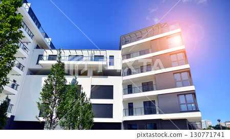 Modern apartment building with balconies and greenery. Beautiful view of real estate buildings in summer. Walking area with trees and grass. Modern residential buildings in the public green area. Modern apartment building with balconies and greenery. Beautiful view of real estate buildings in summer. Walking area with trees and grass. Modern residential buildings in the public green area. 130771741