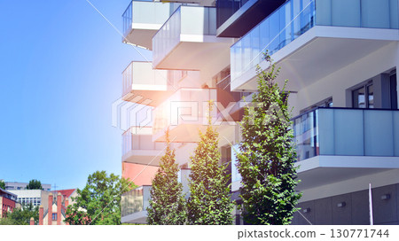 Modern apartment building with balconies and greenery. Beautiful view of real estate buildings in summer. Walking area with trees and grass. Modern residential buildings in the public green area.  130771744