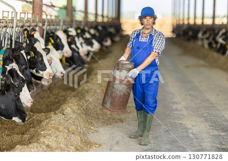 Middle-aged male farmer carrying metal milk tank 130771828