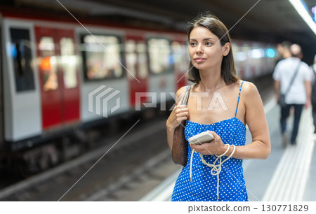 Happy young girl standing on subway platform with phone in hand 130771829