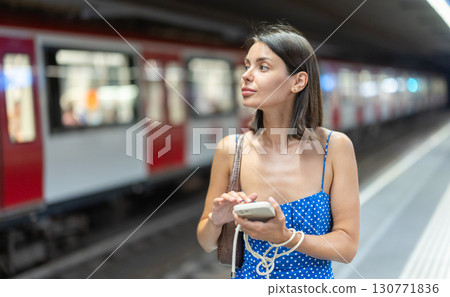 Young girl standing on subway platform with phone in hand 130771836