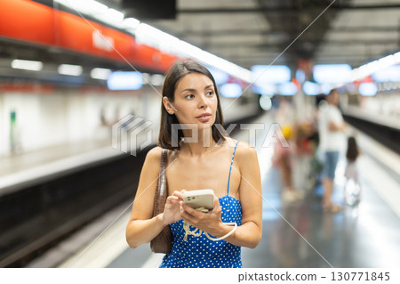 Young girl standing on subway platform with phone in hand Young girl standing on subway platform with phone in hand 130771845