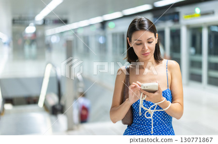 Young girl standing at train station with phone in hand Young girl standing at train station with phone in hand 130771867