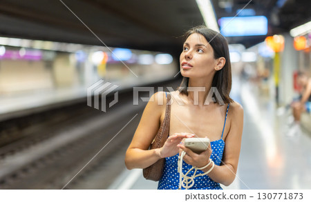 Young girl standing on subway platform with phone in hand 130771873