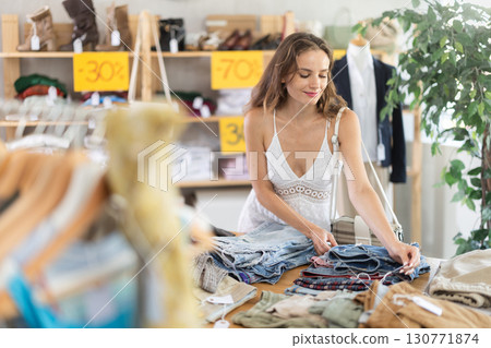 Positive young woman choosing pantaloons in clothing store 130771874