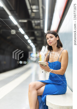 Young woman scrolling phone sitting on platform 130771875