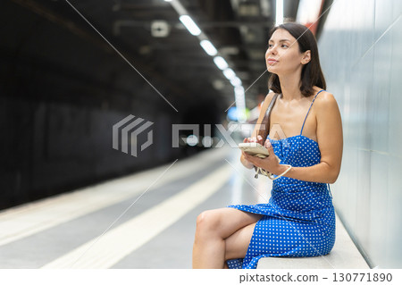 Young woman scrolling phone sitting on platform 130771890