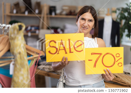 Hostess latin woman holds yellow poster informing about discounts in store. 130771902