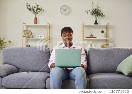 Young African American woman sits on couch with laptop, considering work project or financial issues Young African American woman sits on couch with laptop, considering work project or financial issues 130771930