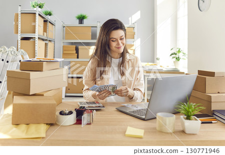Woman Working In Warehouse Or Post Office, Using Laptop And Counting Cash 130771946