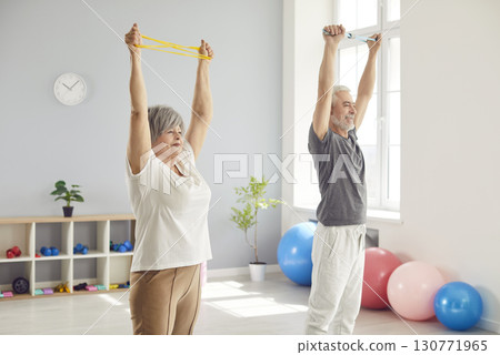 Cheerful senior couple doing stretching exercises and training together during arm rehab in clinic. Cheerful senior couple doing stretching exercises and training together during arm rehab in clinic. 130771965