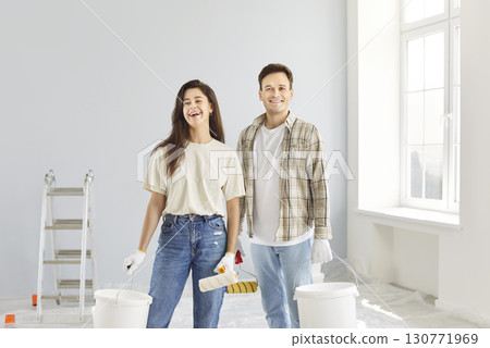 Happy man and woman in gloves holding rollers and buckets of paint 130771969