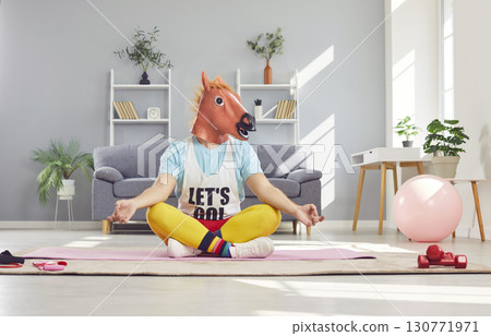 Funny man in sportswear and horse head mask doing yoga exercise sitting on floor in lotus pose. Funny man in sportswear and horse head mask doing yoga exercise sitting on floor in lotus pose. 130771971