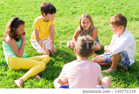 Group of kids resting on grass together and chatting in park 130772134