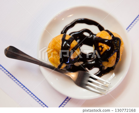 Sweet baked profiteroles with hot chocolate cream at plate 130772168